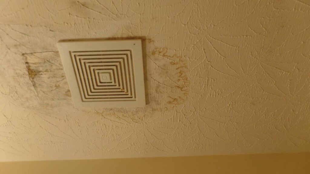 Ceiling vent with water stains and discoloration on textured ceiling, indicating potential water damage or mold issues.