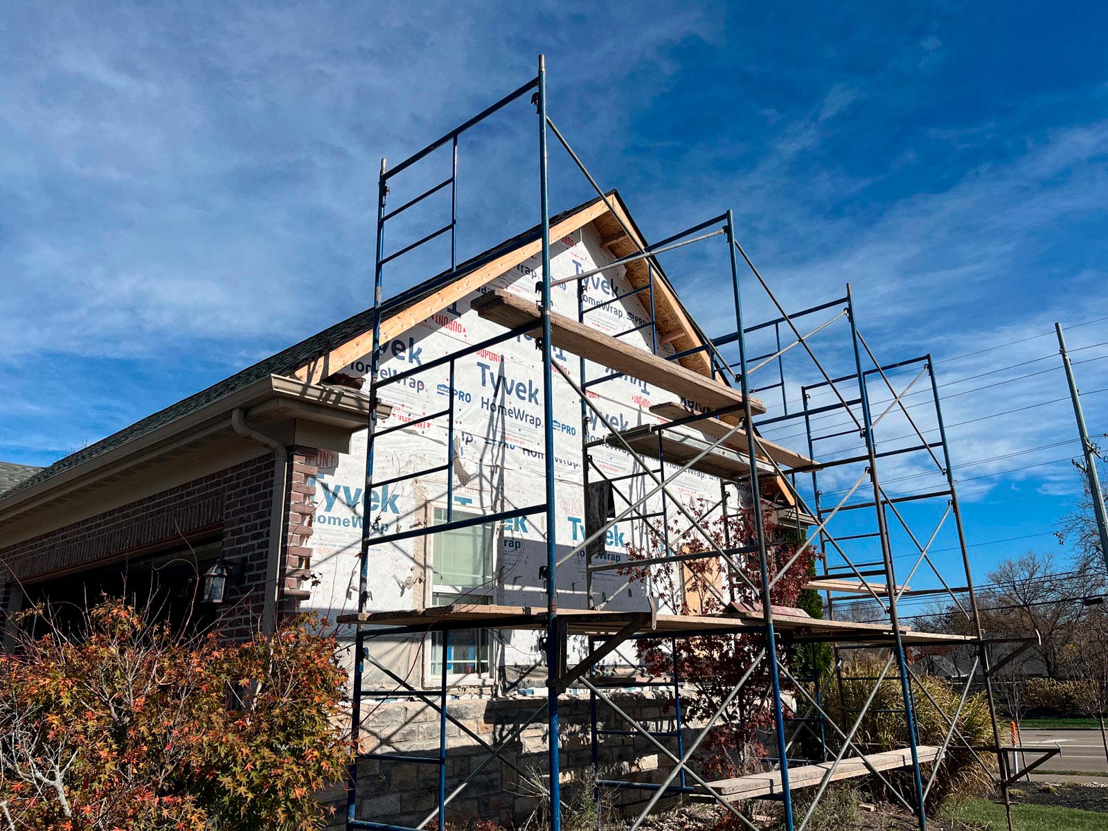 Scaffolding surrounds a house under renovation, wrapped in Tyvek insulation, against a clear blue sky.
